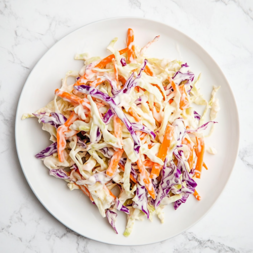 This image shows a vibrant bowl of vegan coleslaw, featuring shredded red cabbage and carrots tossed in a creamy, tangy vegan mayo and apple cider vinegar dressing, perfect for a refreshing side dish.