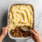 This image shows a golden-brown Shepherd's Pie with a crisp potato topping and a rich, savory meat filling of beef, peas, carrots, and corn, served in a baking dish.