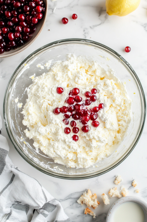A large mixing bowl on the white marble cooktop with milk, lemon zest, vanilla extract, and dried currants stirred into the dry ingredients, forming a thick batter.