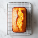The baked clementine yogurt olive oil cake resting on a wire rack placed over the white marble cooktop, cooling and ready to be sliced and served.