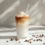 A completed iced coffee in a glass featuring beautifully swirled milk layers, garnished with a straw and surrounded by scattered coffee beans on a white marble cooktop.