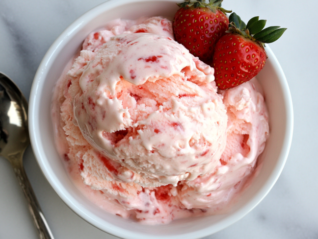 Scoops of creamy homemade strawberry ice cream served in a bowl on the white marble countertop, garnished with a fresh strawberry for a delightful presentation.