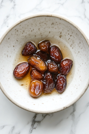 A small bowl on the white marble cooktop contains Medjool dates soaking in warm water for 10 minutes, softening the dates. Afterward, they’re roughly chopped with their soaking liquid for the batter.