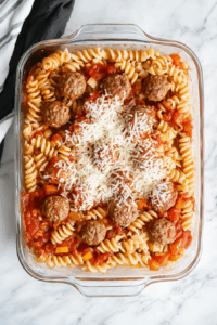 Add uncooked rotini, marinara, water, chopped bell pepper, thawed meatballs, salt, and 1 cup mozzarella to the baking dish.