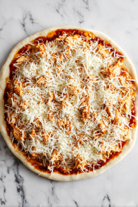 Add the buffalo chicken evenly across the crust. Sprinkle shredded mozzarella cheese on top.