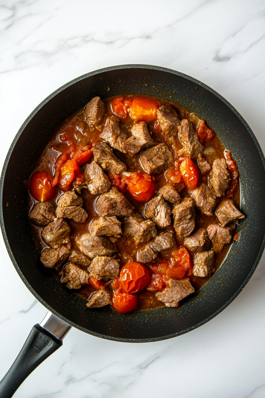 Mix in chopped tomatoes, tomato puree, and lamb stock. Bring to a boil, then reduce heat.