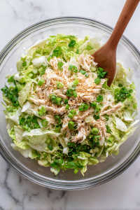 Add shredded chicken, chopped green onions, and toasted sesame seeds to the bowl.