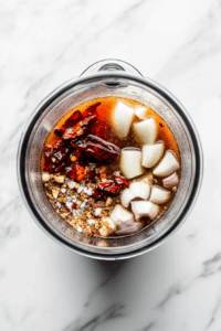 Blend sauce: Blend soaked chiles with garlic, onion, reserved broth, and spices until smooth.