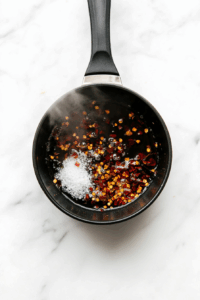 Meanwhile, combine vinegar, salt, sugar, red pepper flakes, and garlic in a saucepan to heat slightly, then pour over carrots and cucumber to pickle.