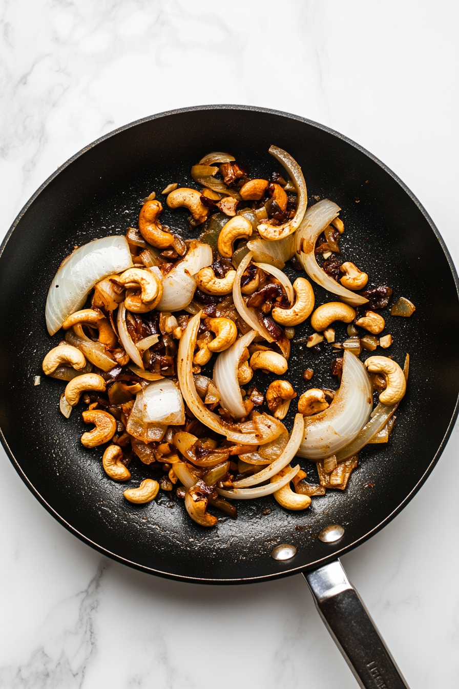 Prepare onion-cashew paste by sautéing sliced onions, ginger, garlic, and soaked cashews until soft; blend into a smooth paste.