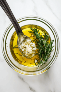 In a small bowl, mix olive oil, minced garlic, and crushed rosemary leaves.
