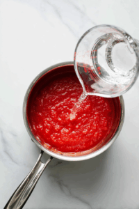 Pour tomato sauce and water into a medium saucepan.