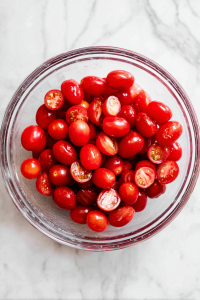 Halve the grape tomatoes and add to a mixing bowl with cucumber.