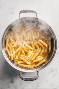 Boil water in a large pot, add salt, and cook the penne pasta until al dente. Drain and set aside.